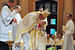 Bishop Christopher J. Coyne, the auxiliary bishop and vicar general, ritually breathes on chrism oil that he then blessed on April 19 during the archdiocese’s annual chrism Mass at SS. Peter and Paul Cathedral in Indianapolis. Assisting Bishop Coyne are, from left, Father Patrick Beidelman, seminarian David Marcotte, transitional Deacon Dustin Boehm (partially obscured) and seminarian Michael Keucher. (Photos by Sean Gallagher)