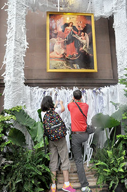 Julie and Doug Bauman, members of St. Barnabas Parish in Indianapolis and teachers at its school, tie strips of paper with prayer intentions onto netting on Sept. 22 below an image of Our Lady, Undoer of Knots at a makeshift shrine dedicated to her beside the Basilica Cathedral of SS. Peter and Paul in Philadelphia. The Baumans participated in an archdiocesan pilgrimage to the World Meeting of Families held in Philadelphia from Sept. 22-25. (Photo by Sean Gallagher) 