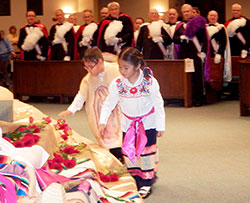 Julian Rodriguez, left, and his sister, Naomi, lay red roses at the feet of a statue of the Blessed Mother during the Dec. 11 solemn vigil Mass for the feast of Our Lady of Guadalupe at Our Lady of the Greenwood Church in Greenwood. (Photo by Mike Krokos)