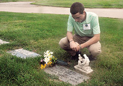 Seminarian Liam Hosty spends time on Aug. 10 before the grave of Father Joseph MacNally at Calvary Cemetery in Indianapolis. Hosty and other archdiocesan seminarians did various works of mercy, including praying for the dead, during their recent annual convocation. Father MacNally was Hosty’s boyhood pastor at St. Barnabas Parish in Indianapolis. (Photo by Sean Gallagher)