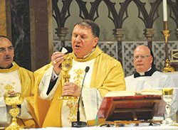 Cardinal Joseph W. Tobin elevates the Eucharist during a Nov. 20 liturgy in the Church of St. Alphonsus Liguori in Rome. Standing behind him is Loral Tansy, master of ceremonies. (Photo by John Shaughnessy) 