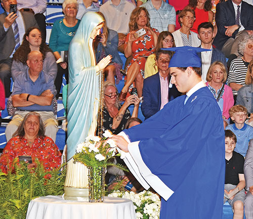 Drew Hasbrook, a member of the Class of 2023 of Bishop Chatard High School in Indianapolis, places a flower in a vase before a statue of the Blessed Mother during the archdiocesan North Deanery high school’s graduation last May. It’s one of the ways the school honors Mary, its patroness, during the month dedicated to her. (Submitted photo)